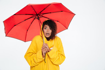 Surprised african woman in raincoat posing with umbrella