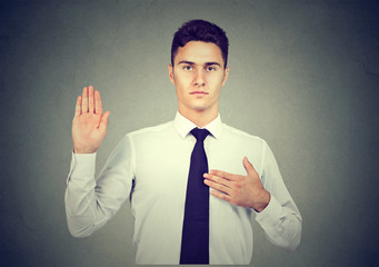 Handsome young business man making an oath promise on gray background