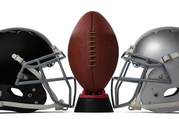 Close up of brown American football on tee by sports helmets