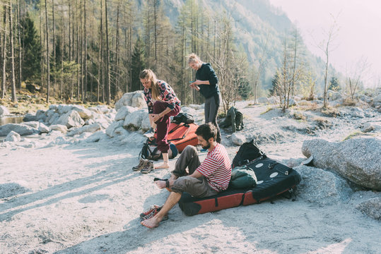 Adult bouldering friends taking off trainers at riverside, Lombardy, Italy