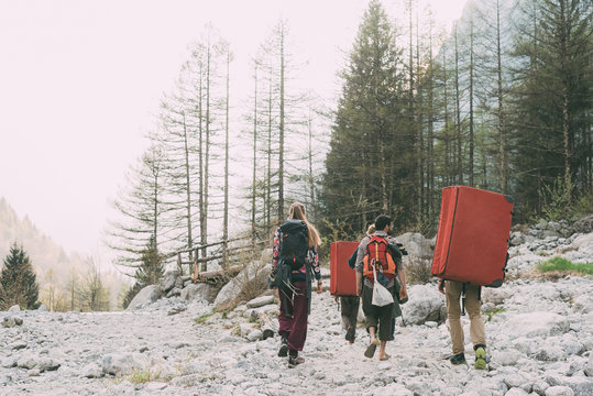 Rear view of adult friends walking near forest with backpack bouldering mats, Lombardy, Italy
