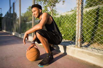 Young man on basketball court, crouching with ball