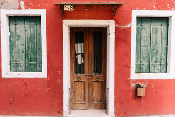 Beautiful colorful house facade on Burano island, north Italy. Red wall with an old wooden door and two windows