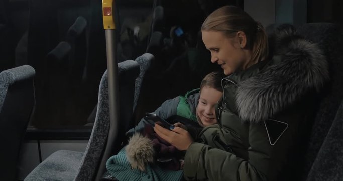 Mom and son having a night bus ride. To pass the time they using mobile. Woman and kid smiling as they looking through the photos