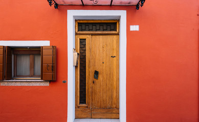 Beautiful colorful house facade on Burano island, north Italy. Minimalistic red wall with a wooden door and a window with open shutters
