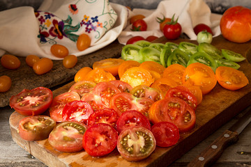 Various different color organic homegrown tomatoes on board. Cut red, yellow, orange and green tomato.