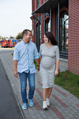 family couple men and  a young pregnant woman walking holding hands and laughing along the city windows