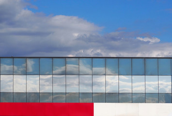Glass facade reflecting the sky with a white and red panel below, under a cloudy blue sky