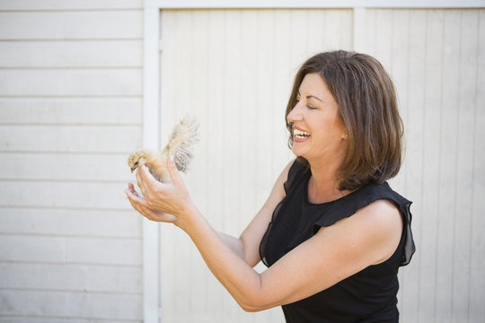 A woman holding a small fluffy chick, a baby bird in her two hands. 