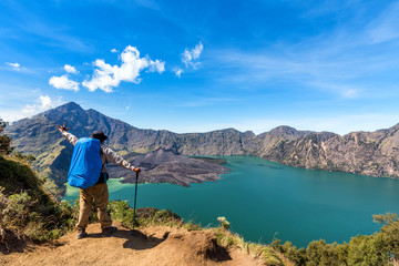 Hiker man with backpack spreading hand, enjoy and happy with active volcano Baru Jari, Lake Segara Anak and summit of Rinjani mountain view after finished climbing at Rinjani mountain.
