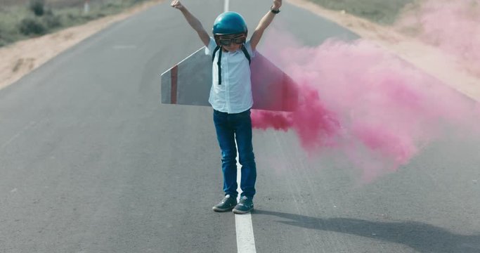 CINEMAGRAPH - seamless loop. Little boy wearing helmet and styrofoam wings standing on a skateboard on a rural road, pretending to be a pilot