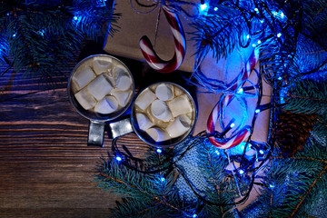 Christmas hot drink. Cocoa with marshmallow, garland and spruce branches on a wooden background. Top view