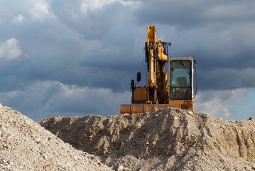 Obraz premium A digger on top of a gravel dune under a cloudy sky