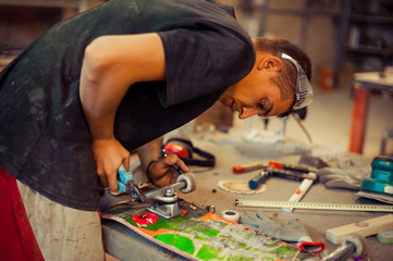 Young man in carpentry workshop fixing wheel on his skateboard