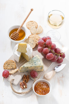 molded cheeses, fruit and snacks on a white wooden board, vertical