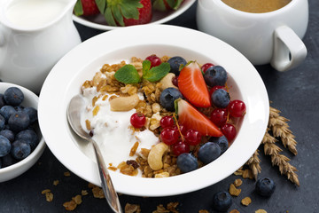 muesli with fresh berries and yogurt for breakfast on a dark background, closeup