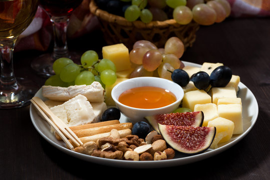 plate of cheeses, snacks and wine on a dark background