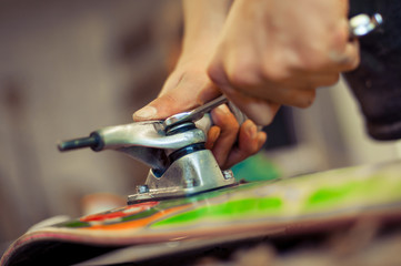 Young man in carpentry workshop fixing wheel on his skateboard