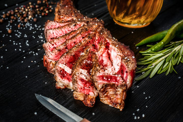 Barbecue dry aged rib of beef with spice, vegetables and a glass of light beer close-up on black wooden background