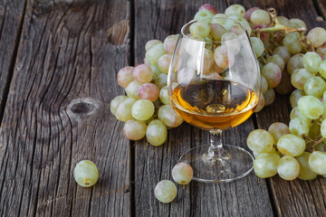 Glass of brandy with brush of grapes on table, harvest holiday