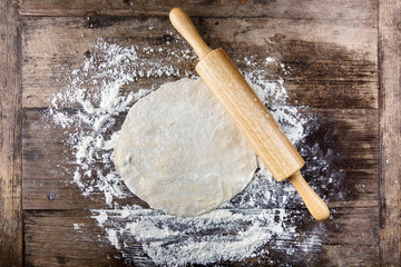 Rolled dough with rolling pin on wooden table covered with baking flour. Pizza cooking background. Text space