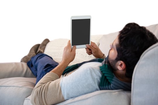 Man lying on sofa while using digital tablet