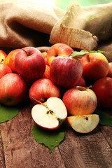 Ripe red apples with leaves on wooden background