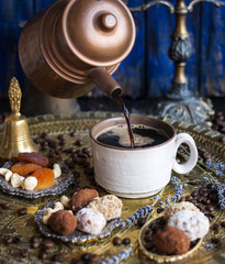 The coffee pot pours the coffee into the cup. in the oriental style. handmade candies, dried fruits and flowers. photo in the style of dark. brassware and ceramics