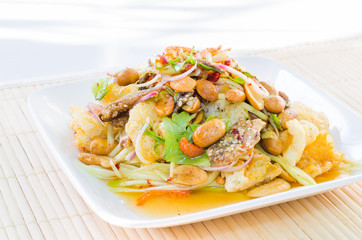 Thai Spicy & Sour Salad with Crispy Fish and Nuts on white plate over bamboo placemat with sun light