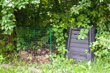 a wireframe and a plastic compost silo under the garden bush
