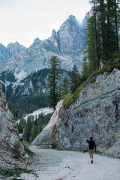 Curious explorer male figure of adventurer nomad traveler walks on path inbetween mountains and forest high in italian dolomites