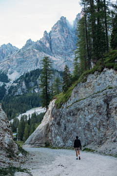 Curious explorer male figure of adventurer nomad traveler walks on path inbetween mountains and forest high in italian dolomites