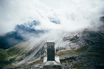 Structure made of stone and bricks to commemorate or signal top of summit on mountain covered with clouds, alps or dolomites, exploration and hiking guide