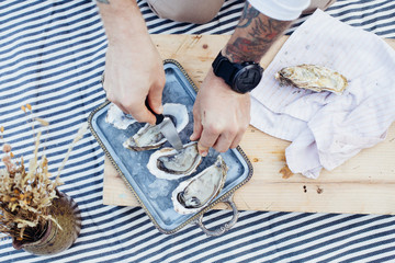 Top view of man preparing fresh organic oysters on top of crushed ice on metal vintage tray, exquisite and delicious seafood, preparation for date