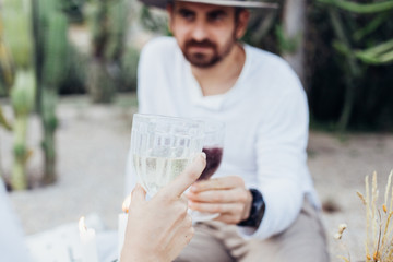 Fototapeta premium Soft focus shot of attractive couple cheering with wine glasses while drinking alcoholic beverages on romantic date. Handsome man with beard smiles and looks at girlfriend