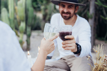 Soft focus shot of attractive couple cheering with wine glasses while drinking alcoholic beverages on romantic date. Handsome man with beard smiles and looks at girlfriend