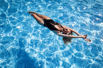 beautiful girl relaxes in the swimming pool in sunny day