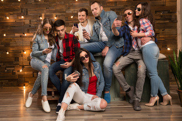 Naklejka na ściany i meble Group of friends happy people, students with smartphones in their hands are watching social networks. Having fun on the Internet online. Positive girls and boys Friendship between men and women.