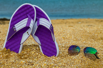 Pair of flip flops and sunglasses on a sandy sea beach
