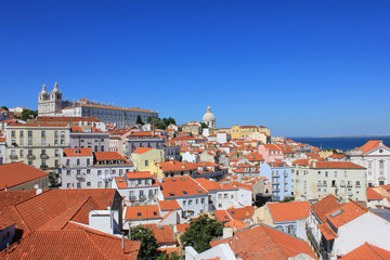 Fototapeta na wymiar Famous portuguese red roofs in Alfama old town historical district on summer time. Miradouro Portas do Sol viewpoint in Lisbon Portugal. Empty clear blue sky and cityscape architecture background