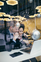 Multi racial business man and woman working together in modern cafe or restaurant. View from street through window glass.