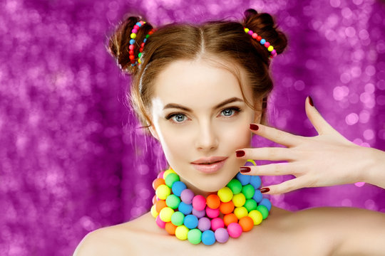 Bright girl model holding hands with manicure on her face. Beautiful, stylish, young woman in a candy doll style with massive beads around her neck