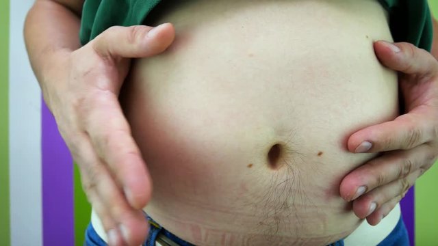 Little fat belly of overweight man. Stomach fat of young obesity male with beer belly. Overweight man shakes belly. Young Adult in jeans pants shakes his fat belly