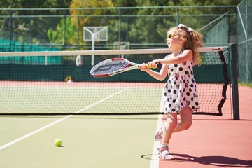 Tuinposter cute little girl playing tennis on the tennis court outside © standret