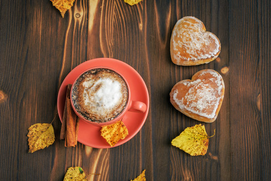 a cup of coffee cappuccino with cinnamon, gingerbread in heart-shaped form, yellow leafy leaves on a wooden table