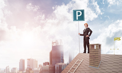 Young businessman with parking sign standing on brick roof. Mixed media