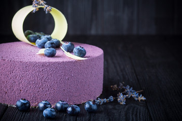 Delicious lavender cake with blueberries on black wooden table