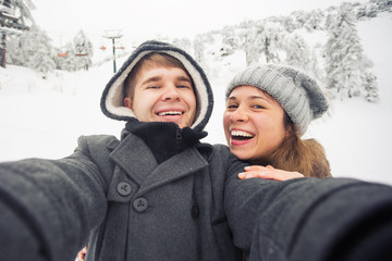 Fototapeta na wymiar people, season, love, technology and leisure concept - happy couple taking selfie by smartphone over winter background
