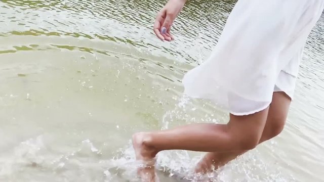 Beautiful woman in white dress are running, jumping and dancing in water in summer