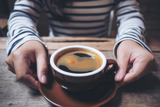 Closeup image of woman's hands holding and giving a cup of hot coffee on wooden vintage table